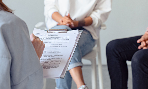 A therapist is writing down things while a couple is talking, sitting down in front of the therapist.
